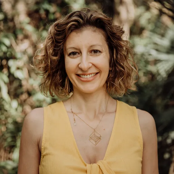 Alison Yanni, a blond woman with short curly hair, with a yellow shirt, smiling at the camera.